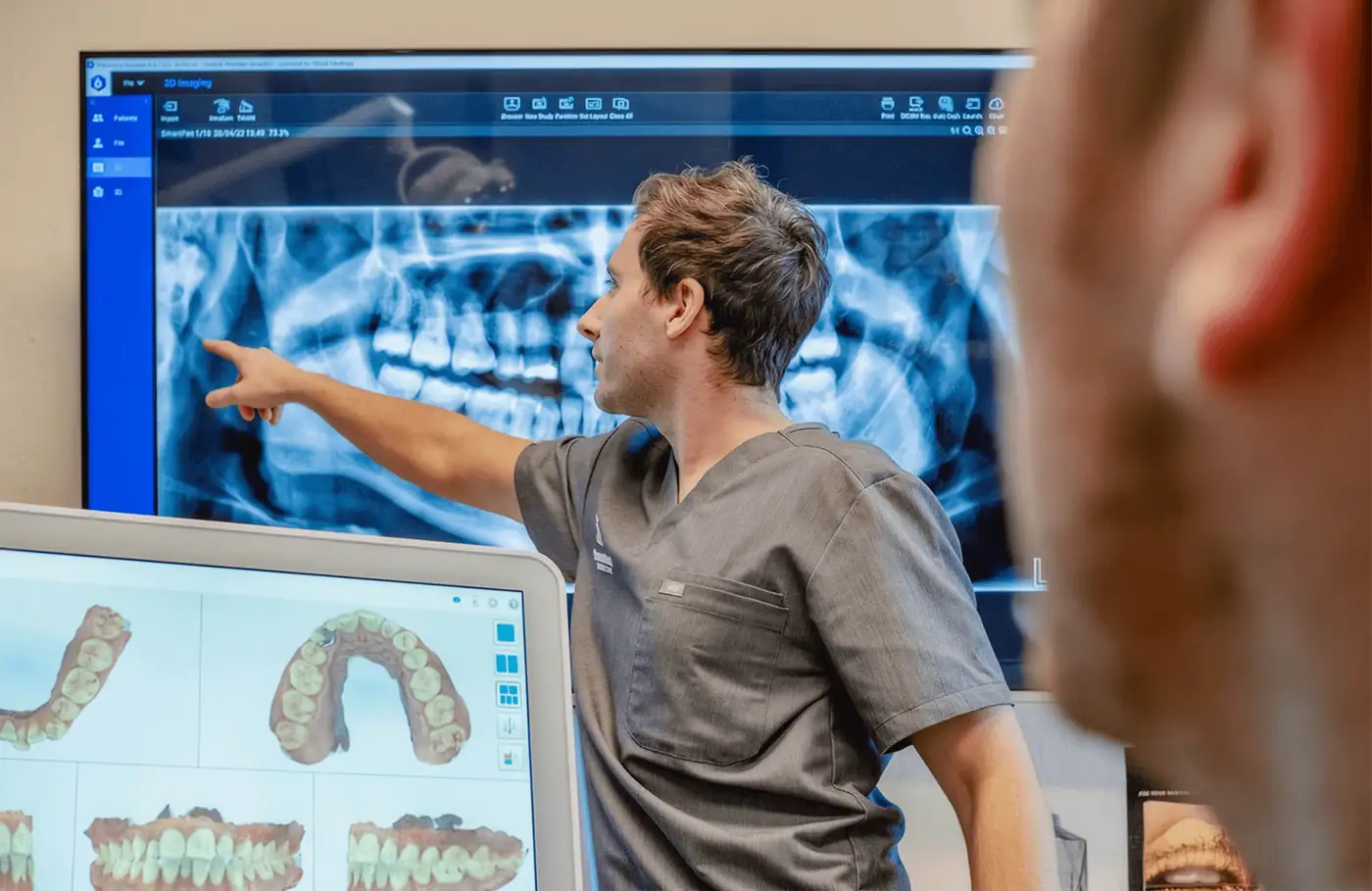 Dentist at QueensWood pointing out a detail on a patient's x-ray on a wall-mounted screen